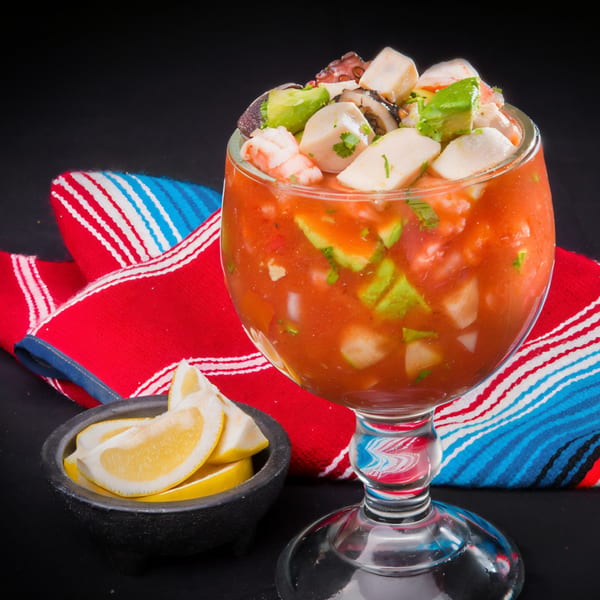 Las Tres Casuelas' seafood cocktail with shrimp, octopus, and avocado in a glass with lemon wedges.