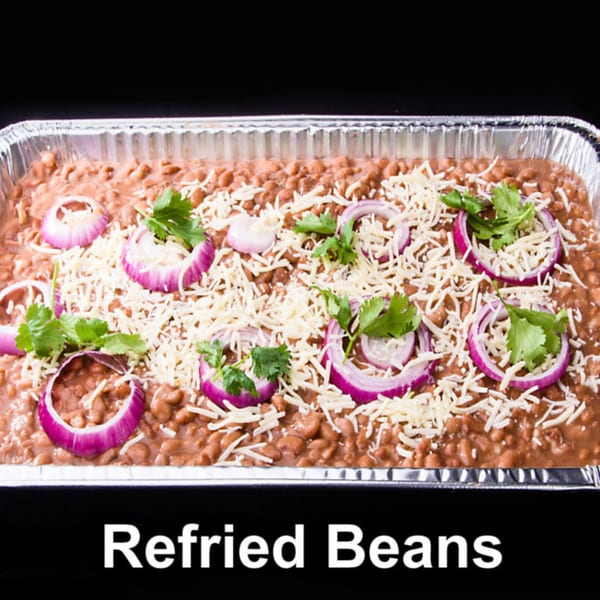 Refried beans in a foil pan, topped with shredded cheese, red onion slices, and cilantro.