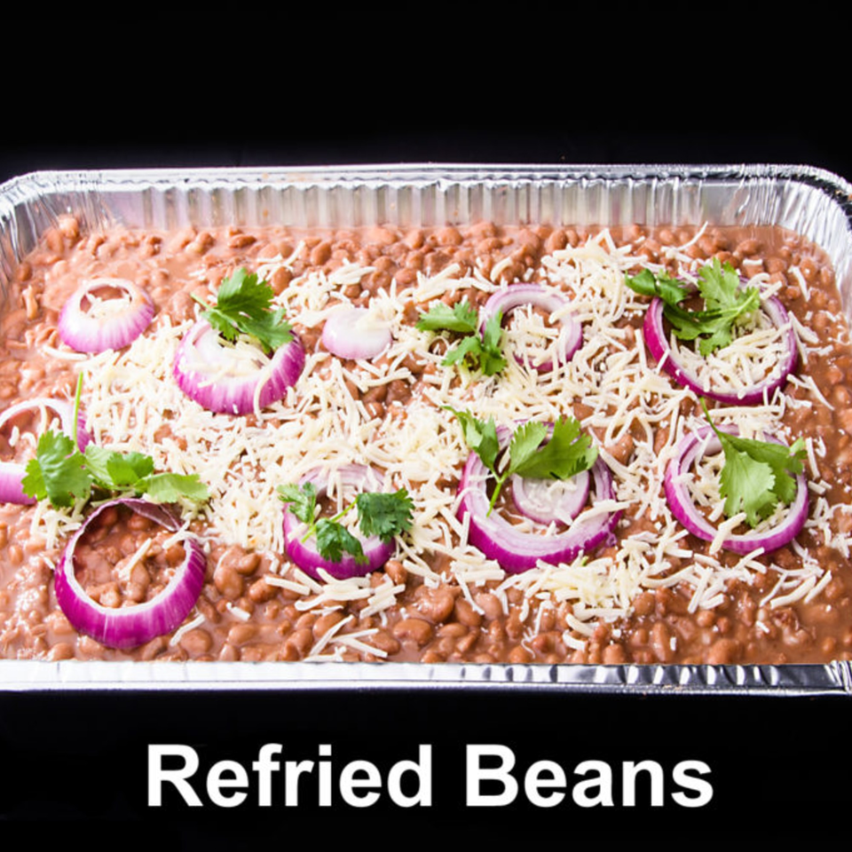 Refried beans in a foil pan, topped with shredded cheese, red onion slices, and cilantro.