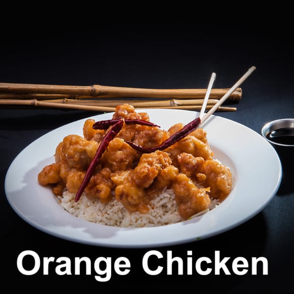 Orange chicken with rice, dried red chilies, chopsticks, and a side of soy sauce.