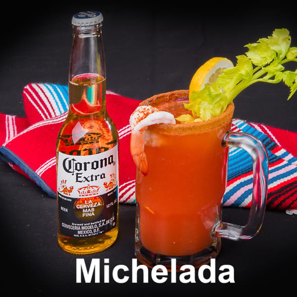 A Corona Extra beer bottle next to a Michelada cocktail garnished with shrimp, lemon, and celery.