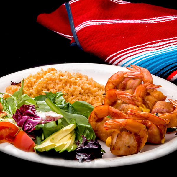 Las Tres Casuelas' grilled shrimp with rice, salad, avocado, and tomatoes on a white plate.