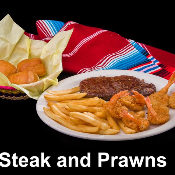 Steak and prawns with french fries and bread rolls, on a plate with a colorful striped blanket.