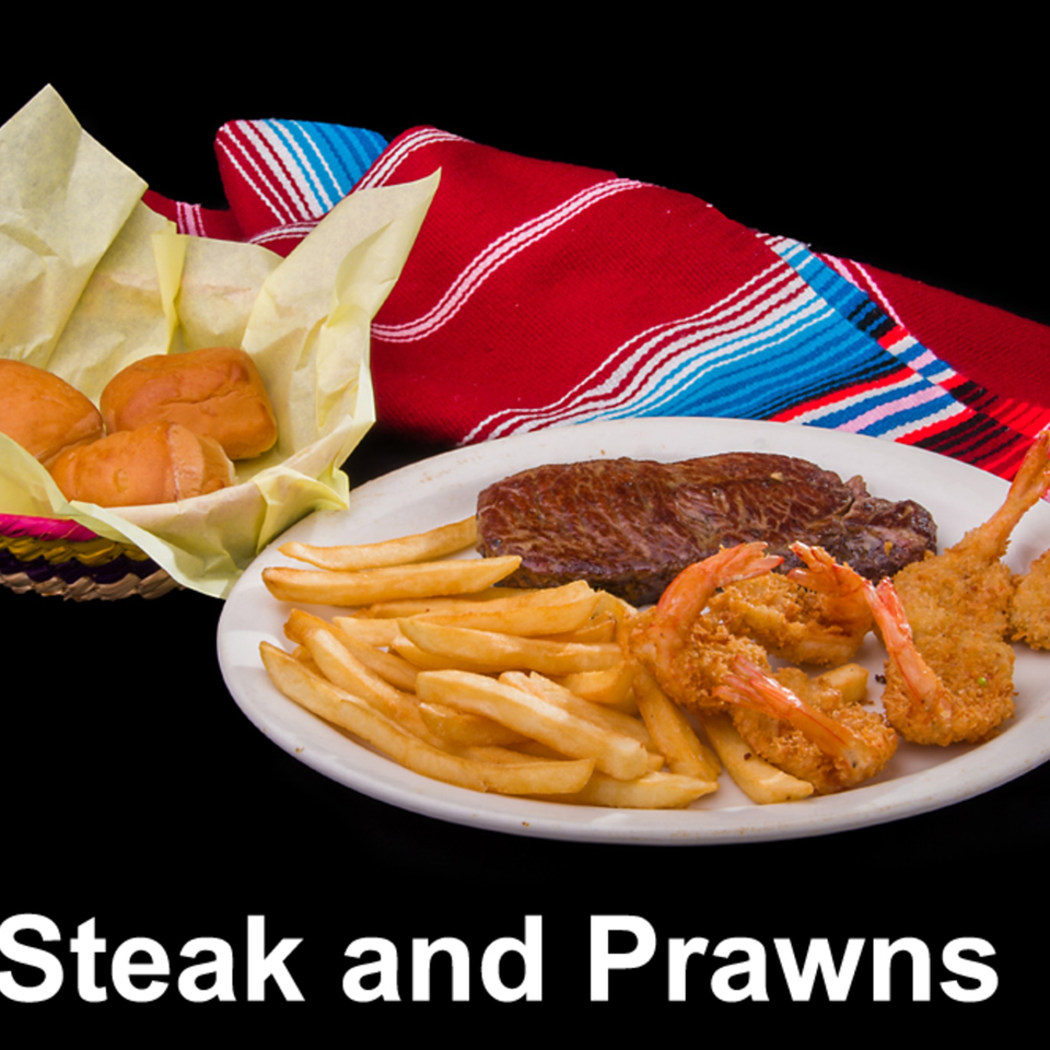 Steak and prawns with french fries and bread rolls, on a plate with a colorful striped blanket.