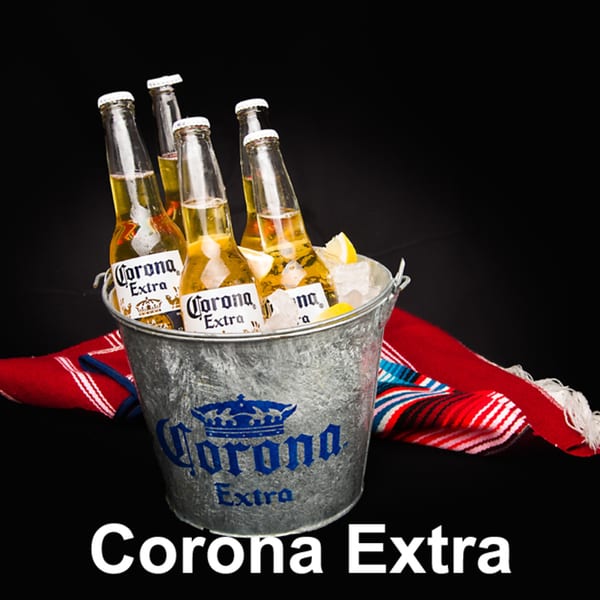 Corona Extra beer bottles in an ice bucket with lemon wedges and a red striped blanket.