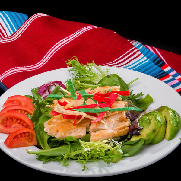 Tex-Mex chicken salad with tomatoes, avocado, and colorful tortilla strips on a white plate.