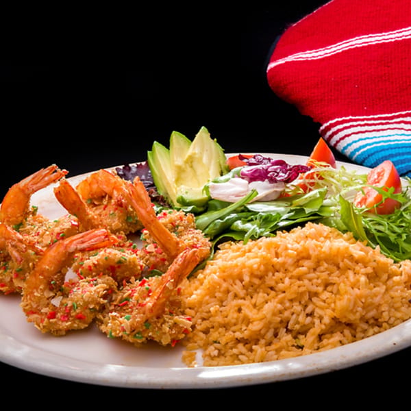 Coconut shrimp with rice, avocado, and salad on a white plate with a colorful striped napkin.