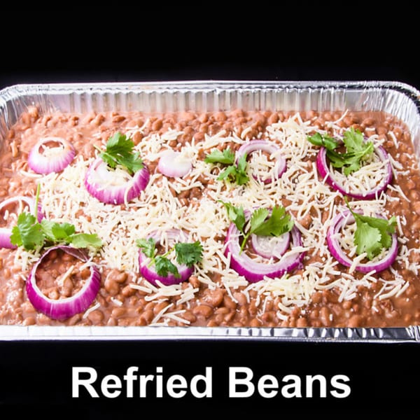 Refried beans in a foil pan, topped with shredded cheese, red onion slices, and cilantro.
