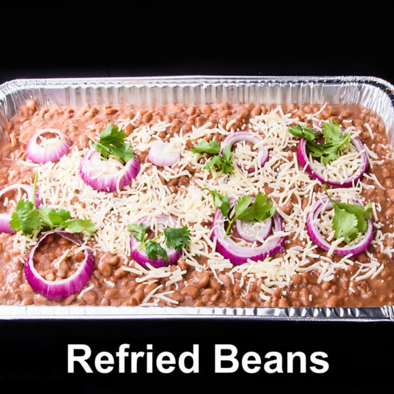 Refried beans in a foil pan, topped with shredded cheese, red onion slices, and cilantro.
