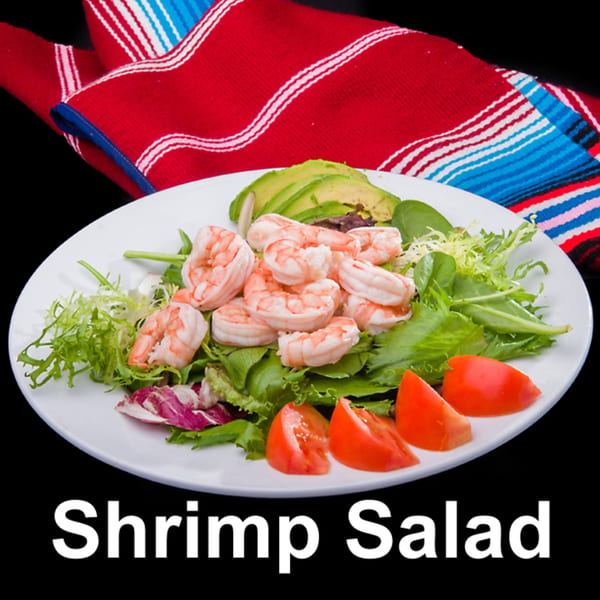 A white plate of shrimp salad with mixed greens, avocado slices, and tomato wedges, on a black background.