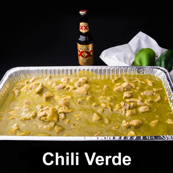Las Tres Casuelas' Chili Verde in a foil pan with a Dos Equis beer and green peppers.