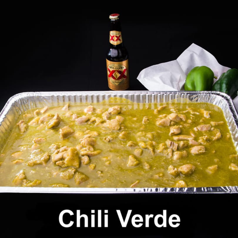 Las Tres Casuelas' Chili Verde in a foil pan with a Dos Equis beer and green peppers.